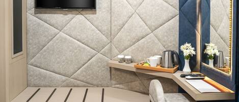 A modern bathroom with a large mirror, a flat-screen TV, a bench, and a vanity with toiletries.