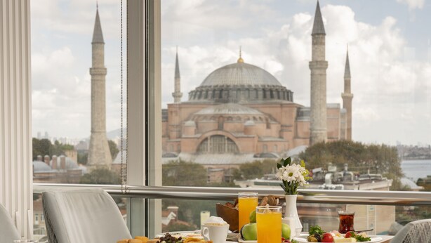 Una mesa de desayuno con diferentes platos, un vaso de zumo de naranja y vista a una mezquita con minaretes.