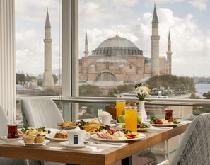 Ein Frühstückstisch mit verschiedenen Speisen, einem Glas Orangensaft und Blick auf eine Moschee mit Minaretten.