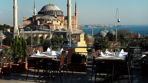 Un restaurante con terraza al aire libre, frente a un edificio histórico con cúpulas y minaretes.