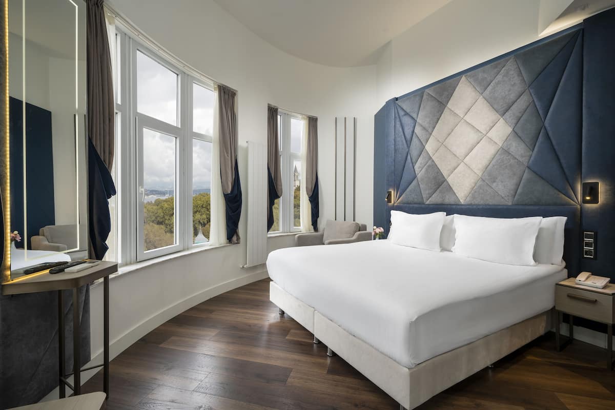 Ein modernes Hotelzimmer mit einem großen Bett, einem Nachttisch, einem Spiegel und Blick ins Freie.