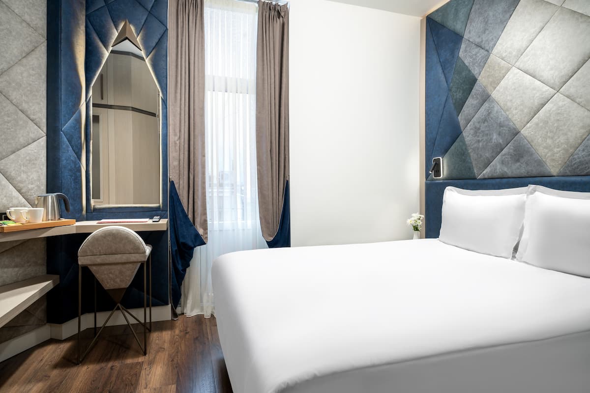 Ein Hotelzimmer mit Bett, Schreibtisch mit Stuhl, Spiegel und einem Fenster mit Vorhängen.