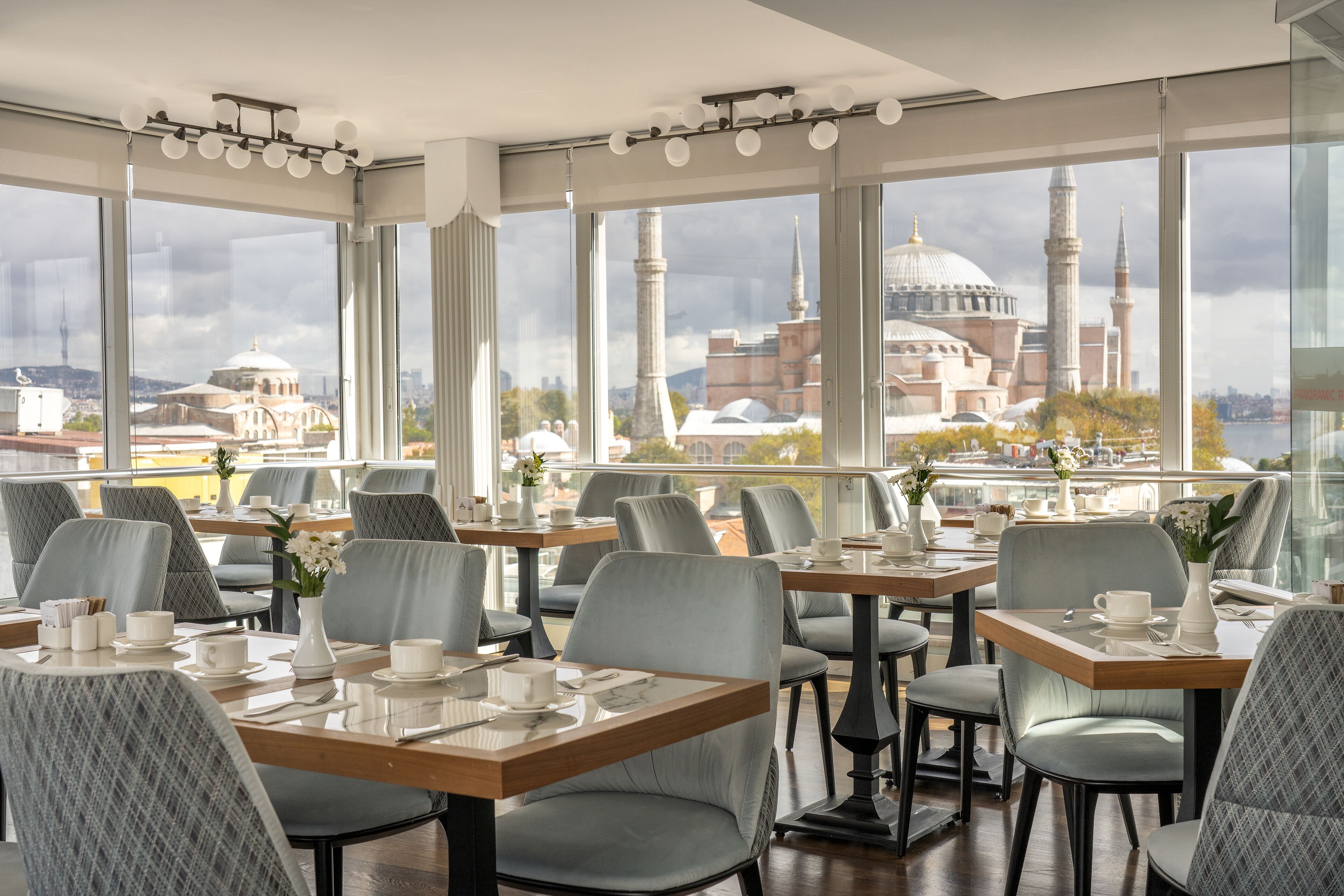 A restaurant with tables set for dining, large windows offering views of historic buildings.