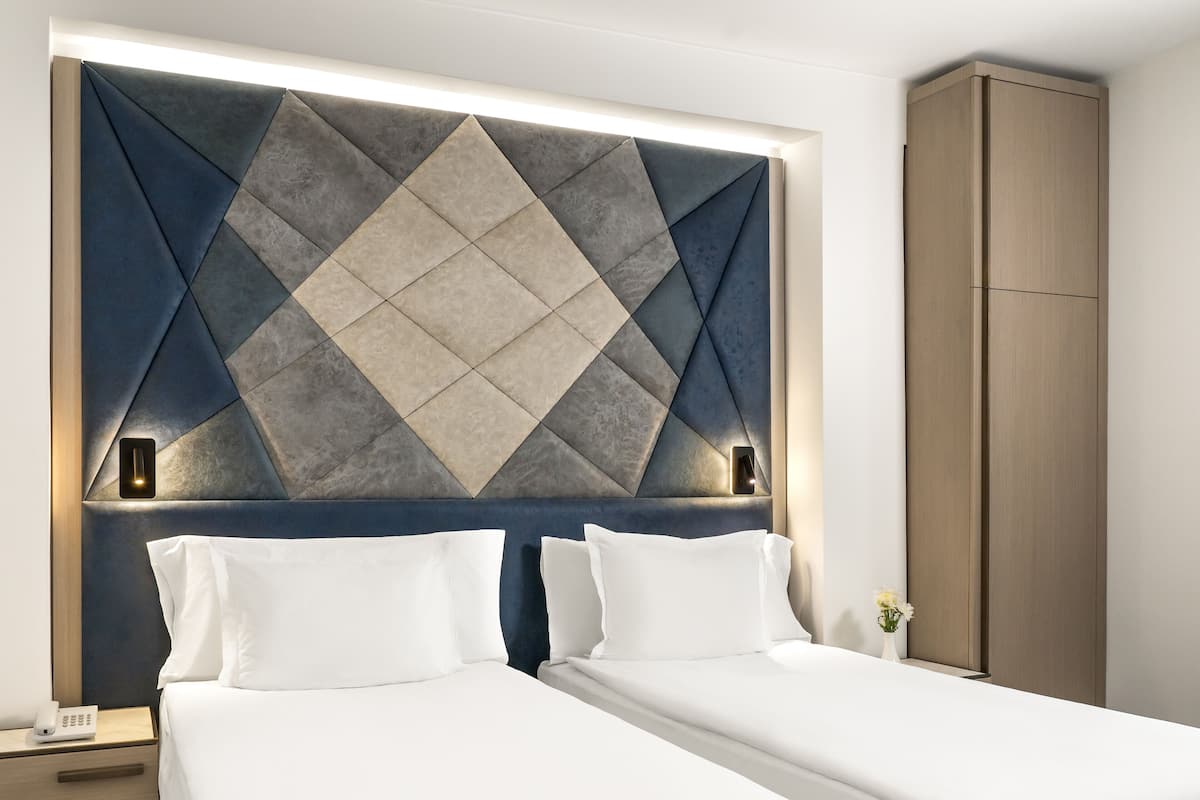 Ein Hotelzimmer mit zwei Einzelbetten, einem Nachttisch mit Telefon und einem Kleiderschrank.