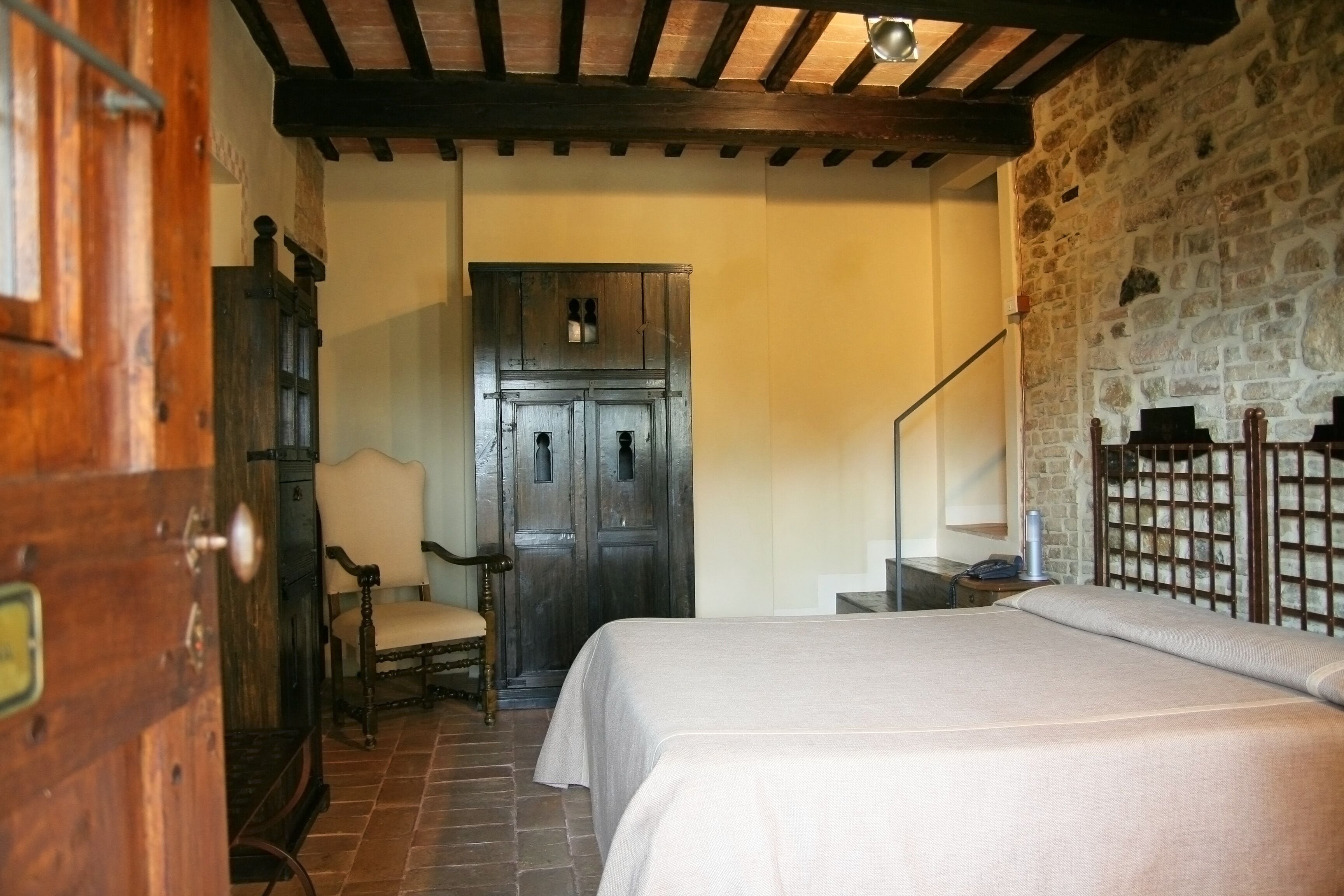 Un dormitorio con una cama, un armario de madera, una silla y una pared de piedra.