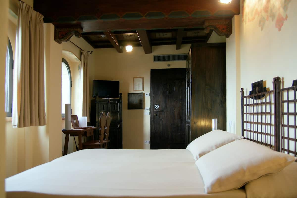 A hotel room with a large bed, wooden headboard, a desk with a chair, a television, and a wardrobe.