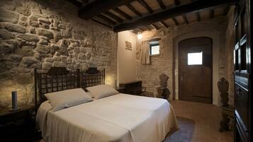 A bedroom with a stone wall, a wooden bed frame, a nightstand, and a small window with curtains.