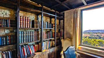 Ein Zimmer mit einem großen Bücherregal voller Bücher, einem Ledersessel und einem Fenster mit Blick auf eine Landschaft.