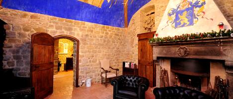Una habitación de paredes de piedra con chimenea, candelabro y un sillón de cuero.