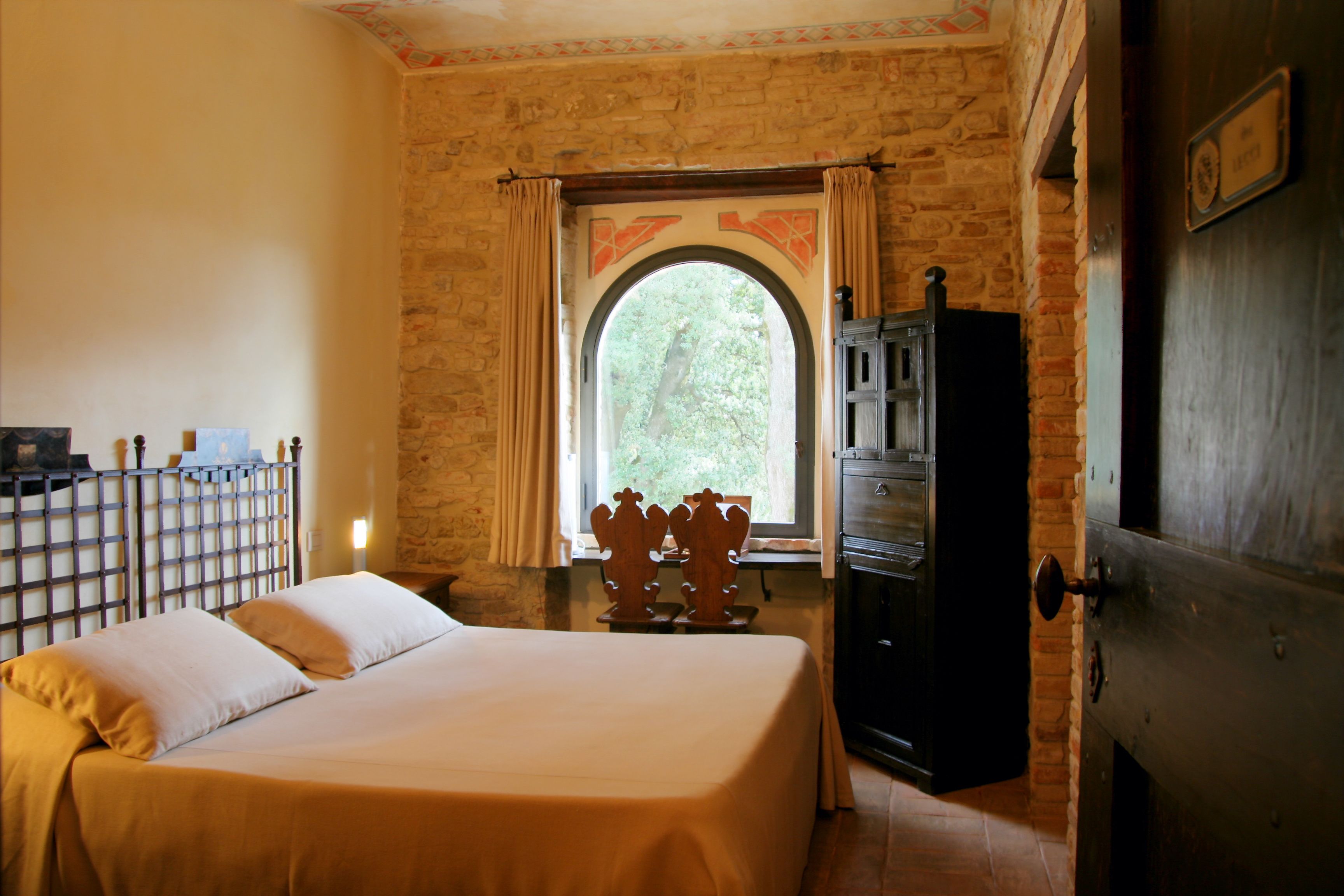 A bedroom with a bed, a window with curtains, a wooden cabinet, and a brick wall.