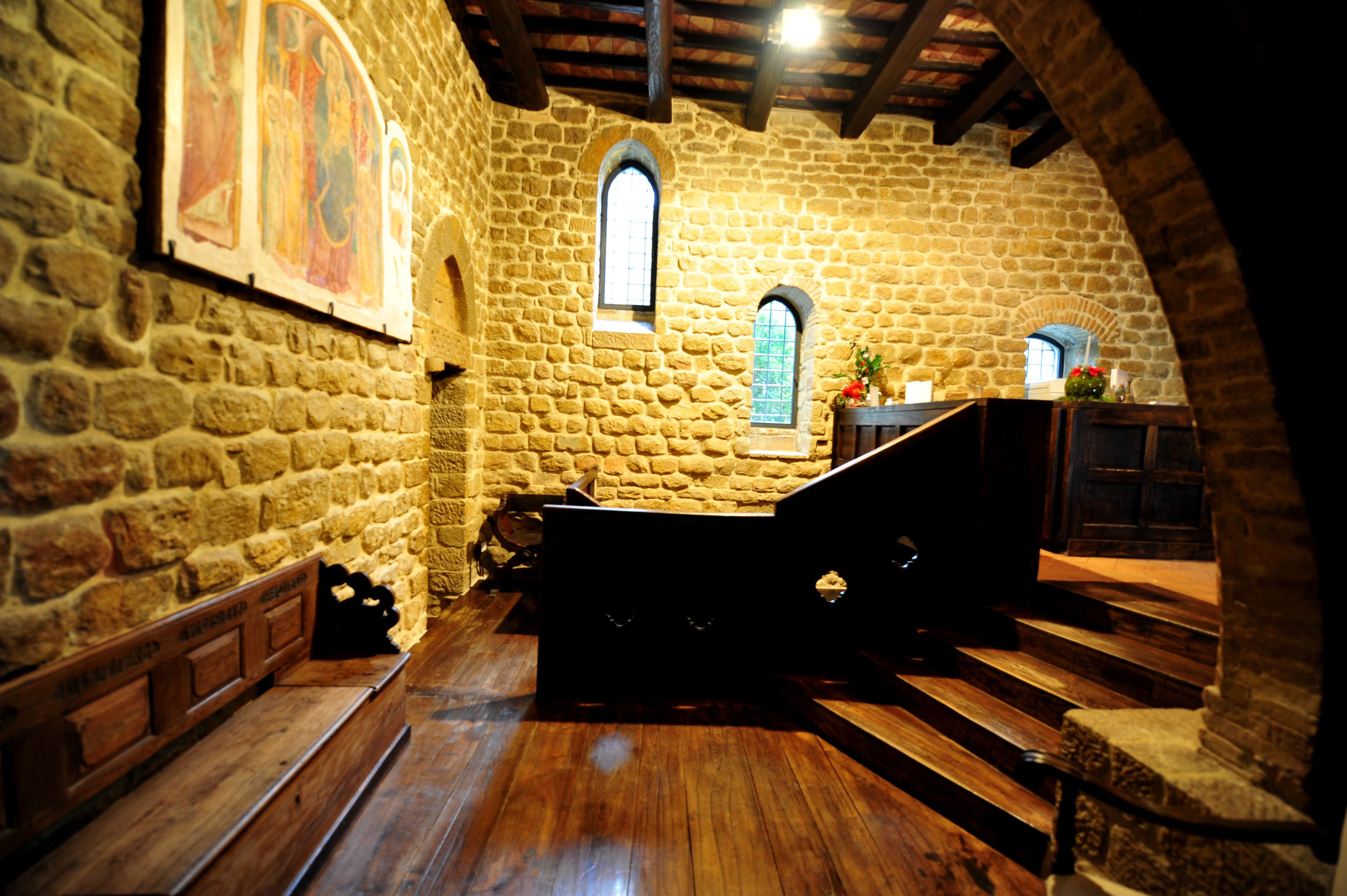 Interior de parets de pedra amb bancs de fusta i una escala.