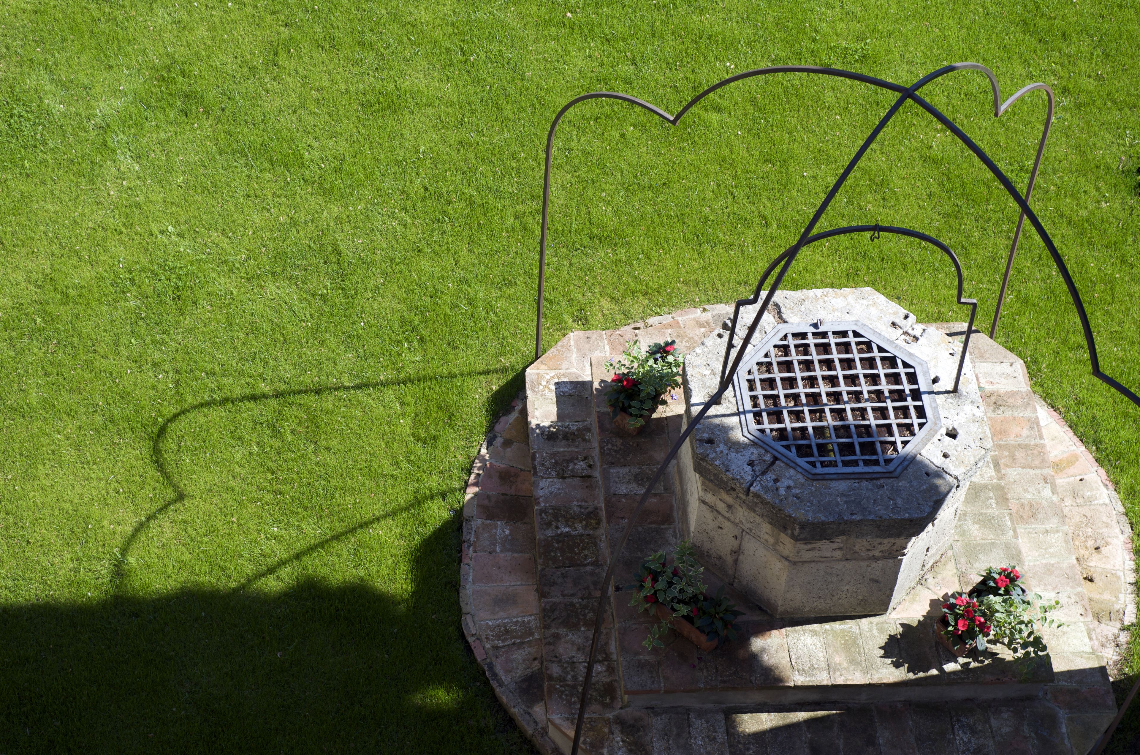 A stone structure with a metal grate, surrounded by a circular stone base, and potted plants with red flowers.
