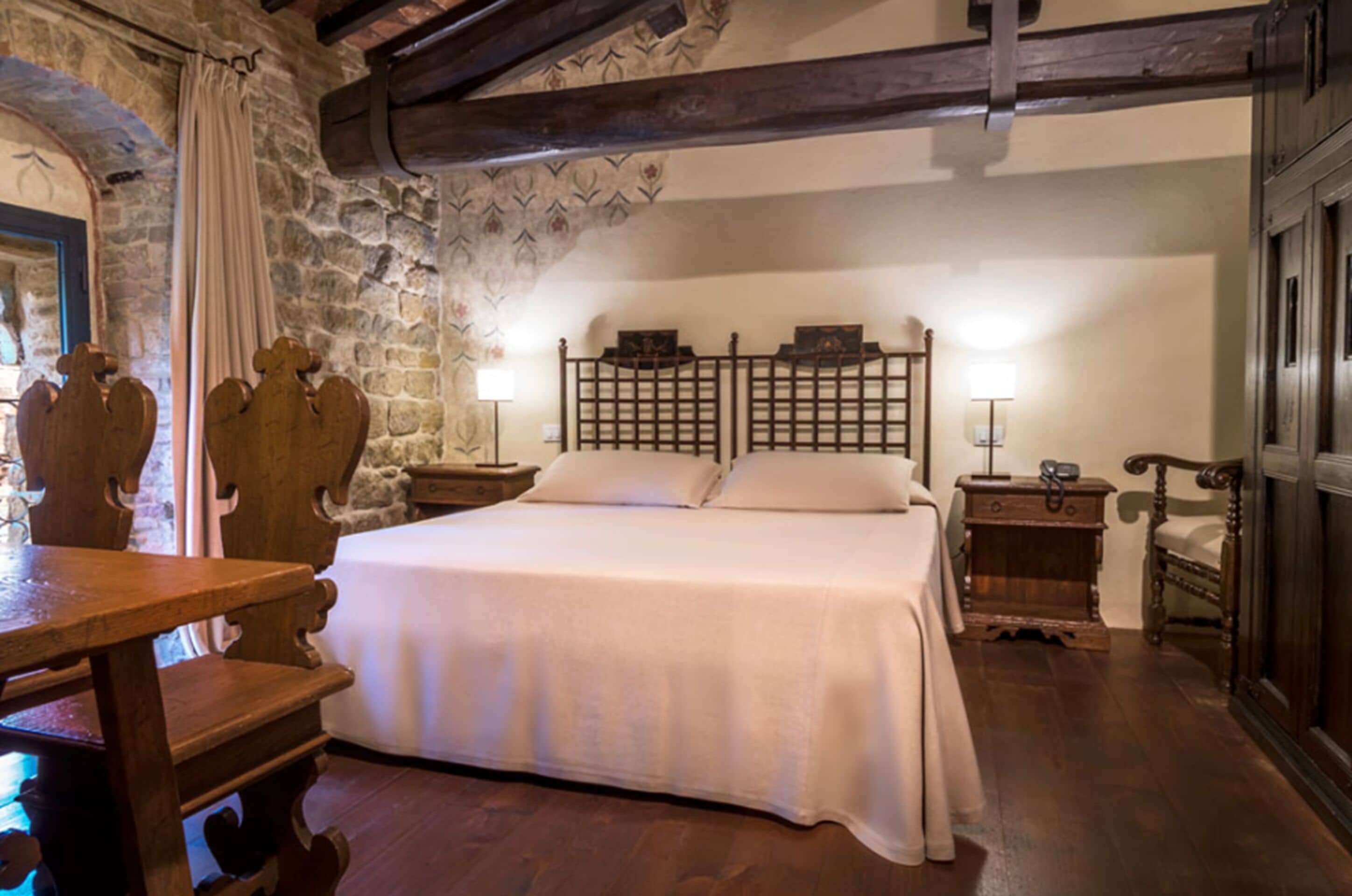 A bedroom with a large bed, wooden headboard, stone walls, and a wooden table with chairs.