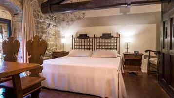 A bedroom with a large bed, wooden headboard, stone walls, and a wooden table with chairs.
