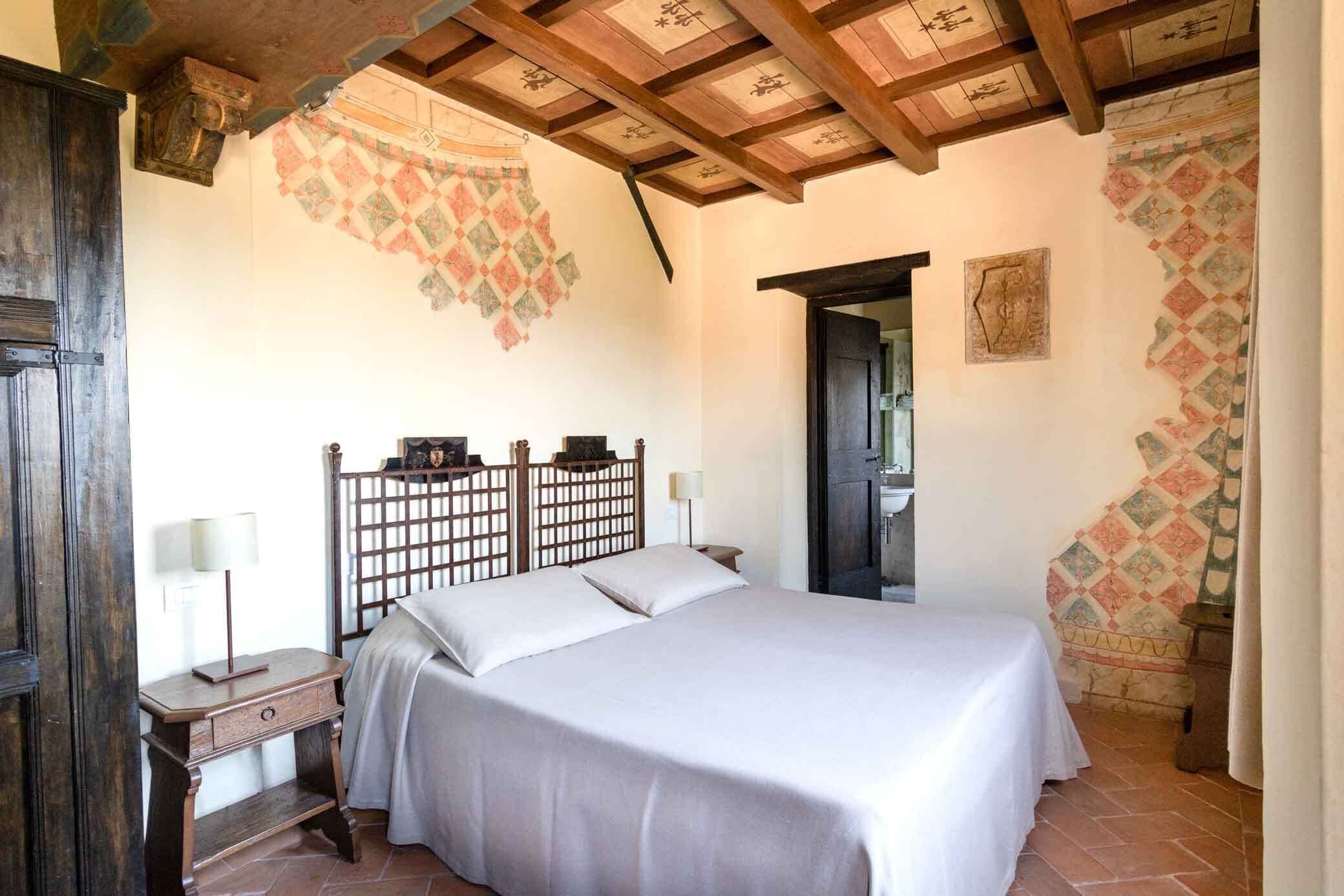 A bedroom with a wooden bed, a nightstand, a wall-mounted shelf, and a door leading to another room.