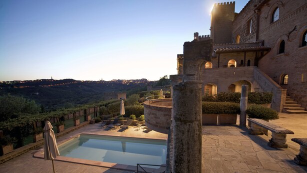 A courtyard with a pool, stone benches, and a view of a hill. - TH Perugia - Castello di Monterone (Perugia)