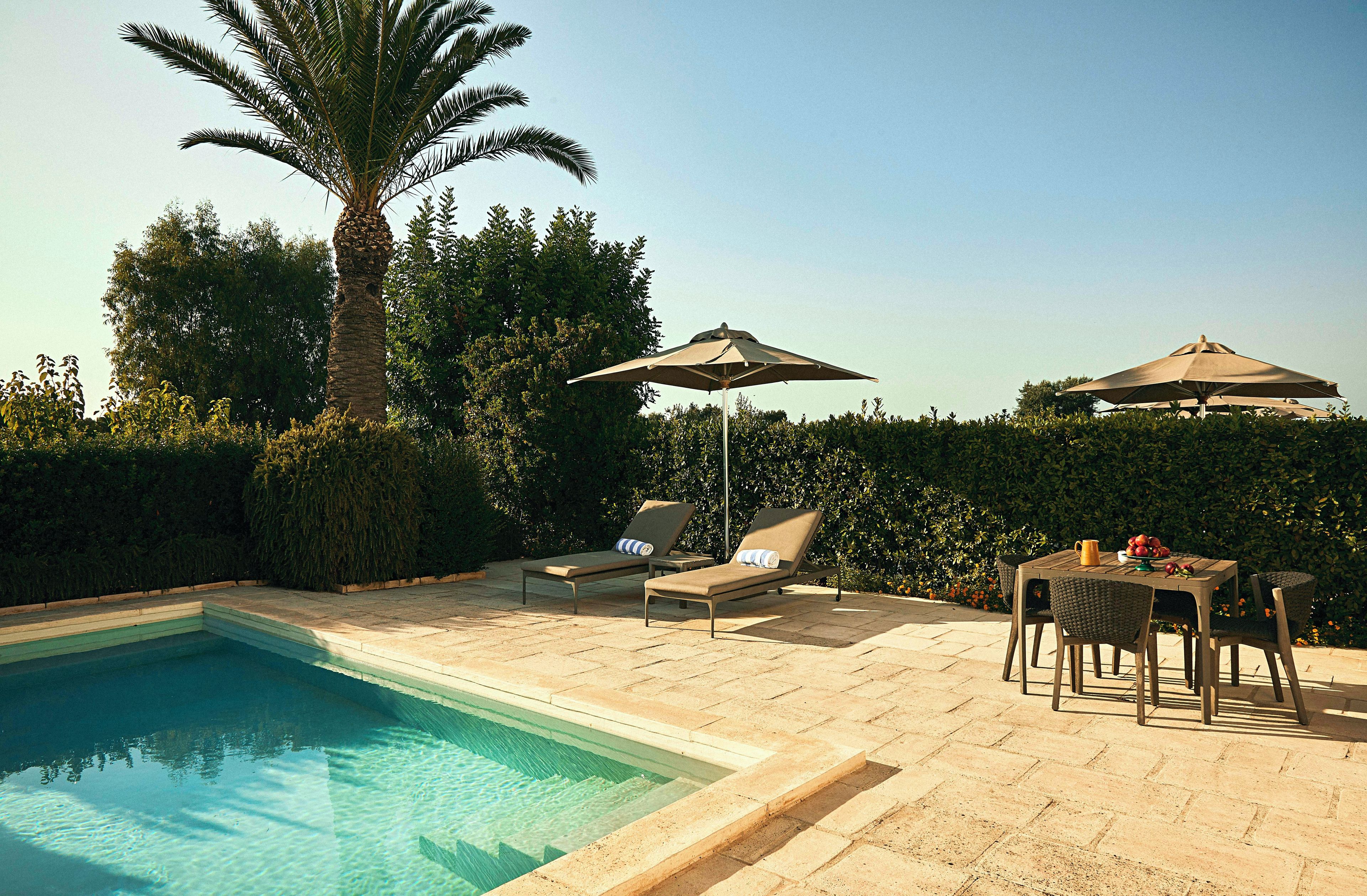 Area piscina con lettini, ombrelloni e un tavolo con frutta.