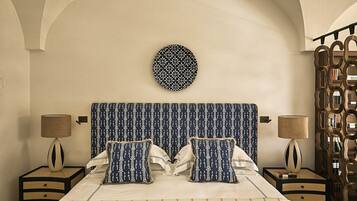 Un dormitorio con un cabecero estampado, dos mesitas de noche con lámparas, un adorno en la pared y una colcha con diseño.