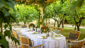 Un área de comedor al aire libre con mesas redondas cubiertas de manteles blancos, rodeada de sillas de mimbre.