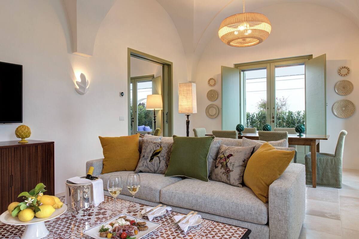 Ein modernes Wohnzimmer mit Sofa, Esstisch und Stühlen. An der Wand befindet sich ein Fernseher und ein Fenster mit Blick ins Grüne.
