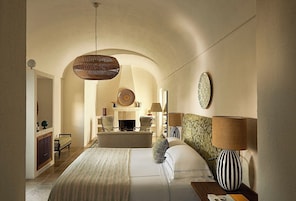 A spacious bedroom with a large bed, a hanging light fixture, and a fireplace.