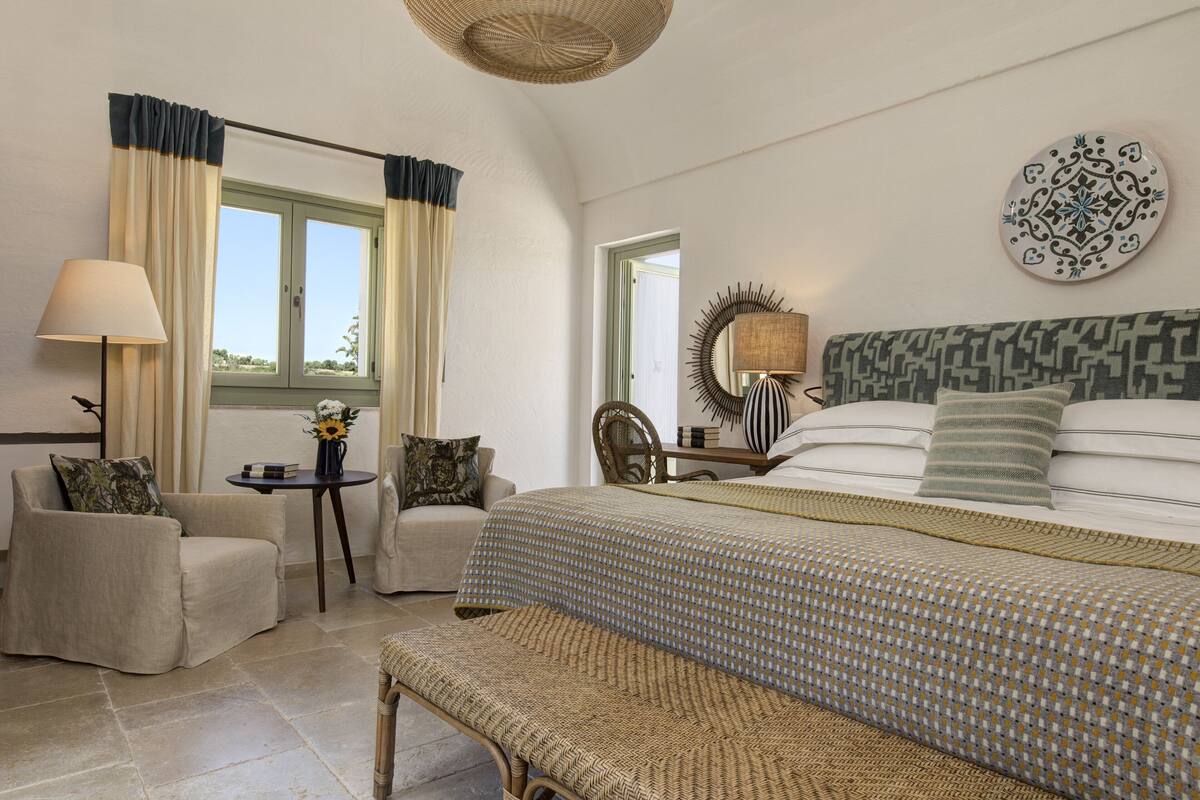 Ein Schlafzimmer mit einem Bett, einem Sessel, einem Tisch und einer Lampe.