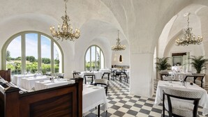 Un restaurante con techos altos en arco, candelabros y suelo a cuadros. Las mesas están dispuestas con manteles blancos y sillas.
