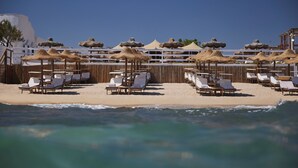 Un resort frente a la playa con tumbonas y sombrillas de paja, una valla de madera y una vista despejada del océano.