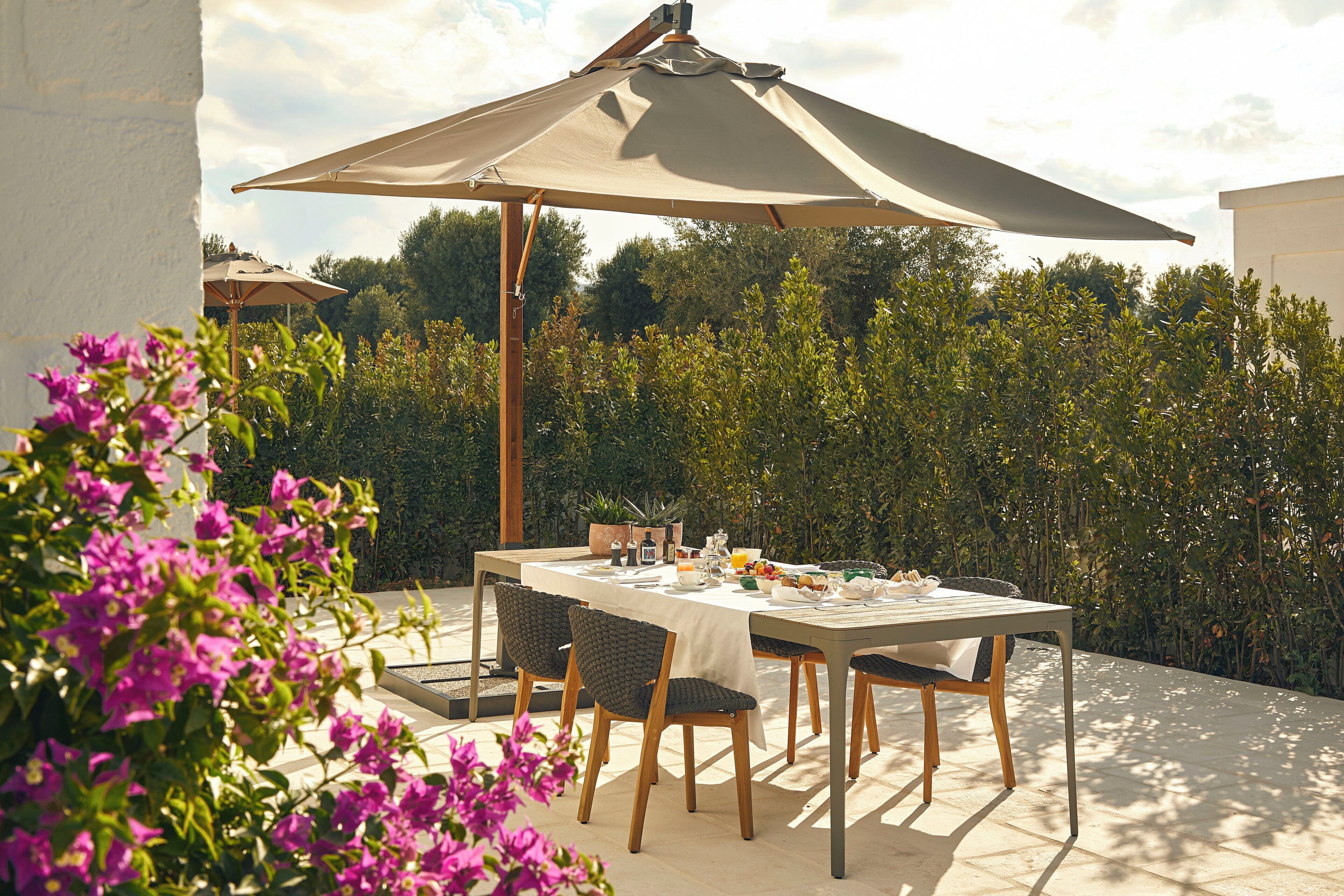 An outdoor dining area with a table set for breakfast, surrounded by chairs and an umbrella.