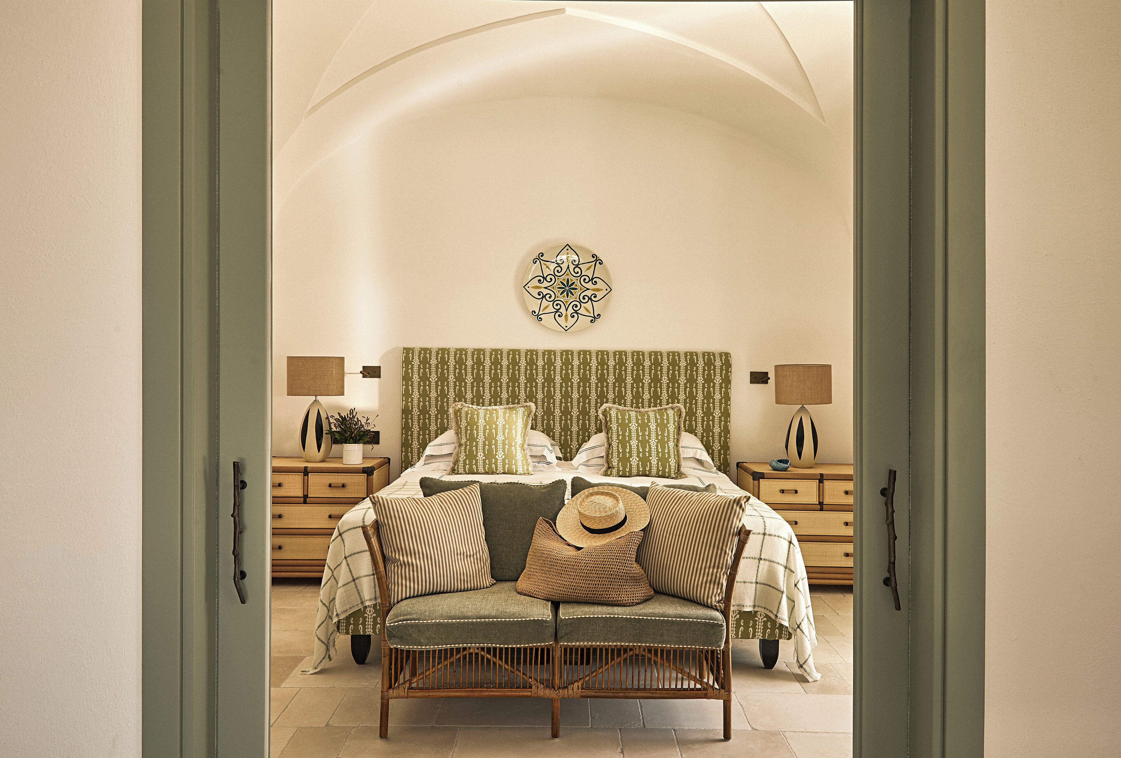A bedroom with a bed, a bench, a hat, and a decorative wall piece.