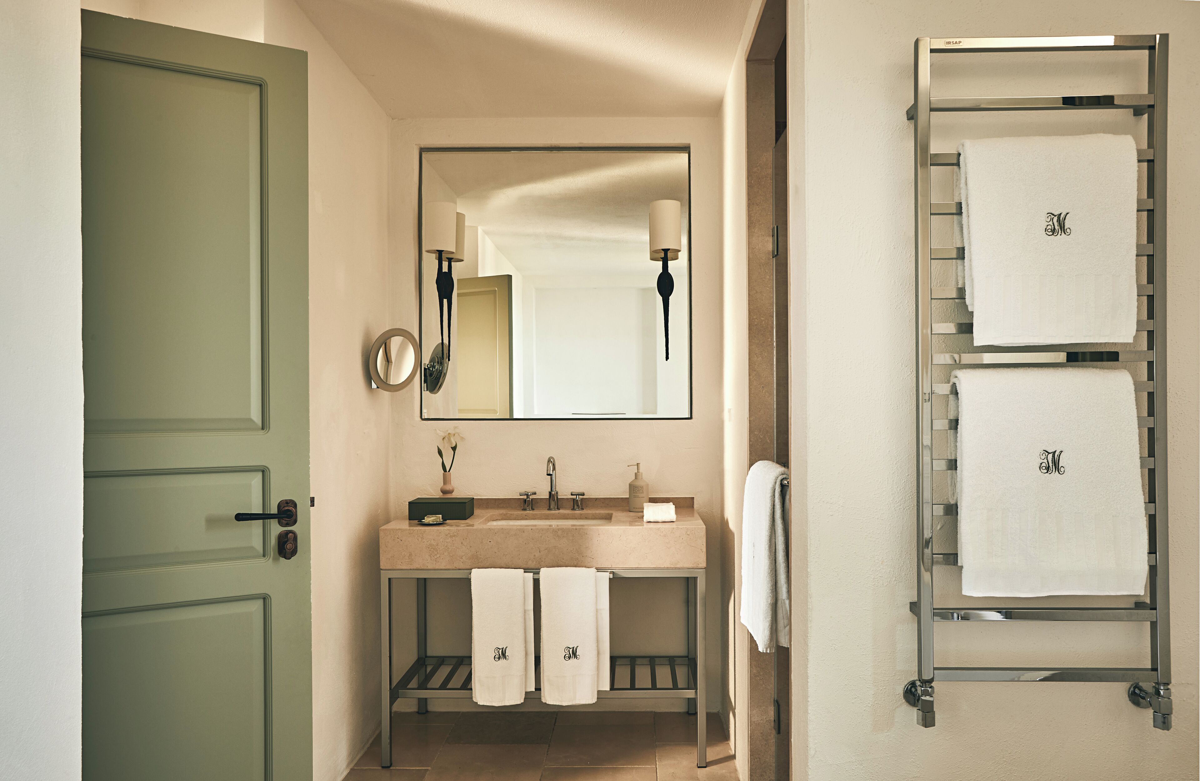 Une salle de bain avec une porte verte, un lavabo avec deux serviettes, un miroir et un porte-serviettes avec trois serviettes.