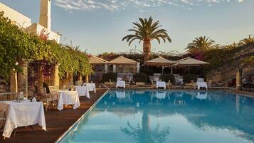 A poolside area with tables and chairs, a palm tree, and a building with a tower.