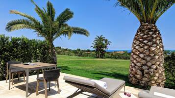 A patio with a table and chairs, a lounge chair, and a palm tree.
