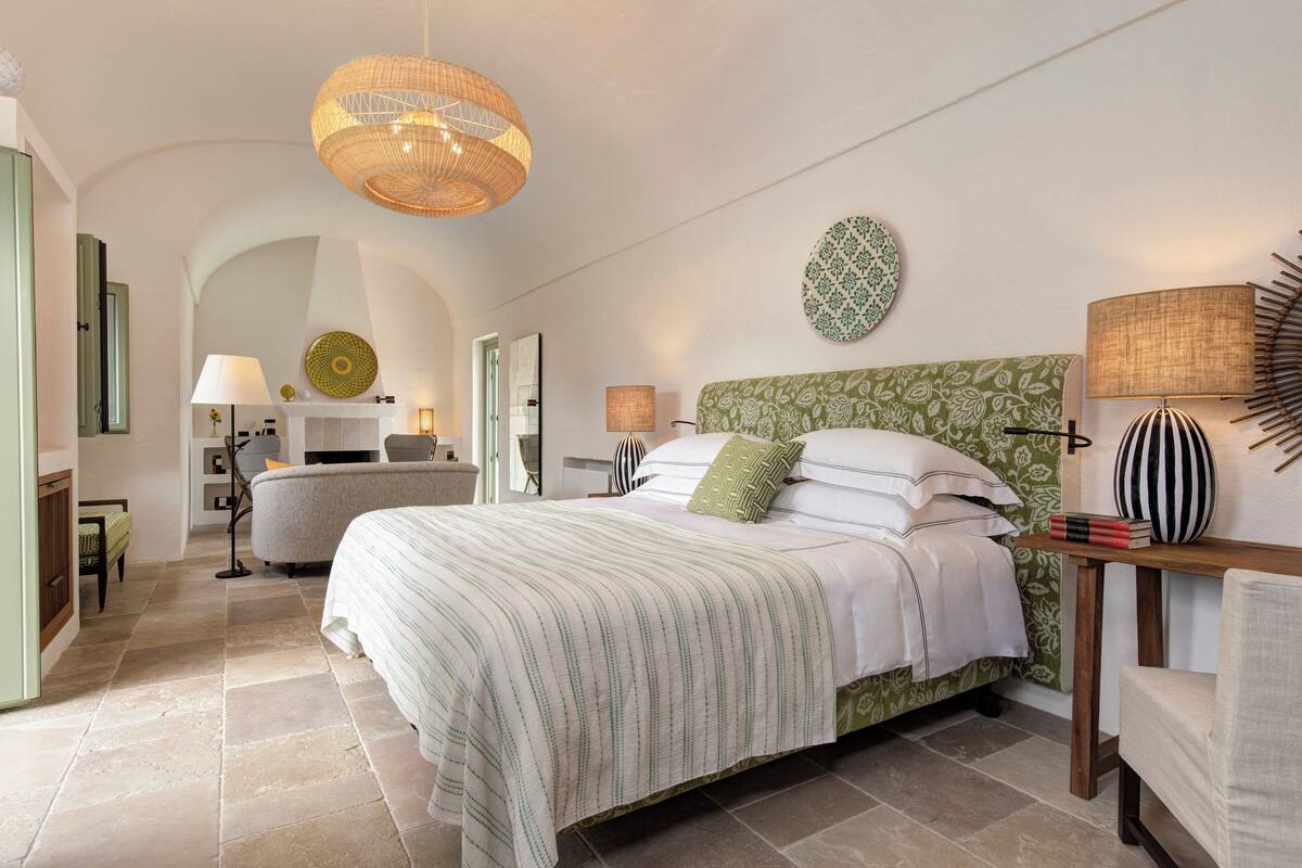 Ein helles Schlafzimmer mit einem großen Bett, einem grün gemusterten Kopfteil und einer Pendelleuchte.