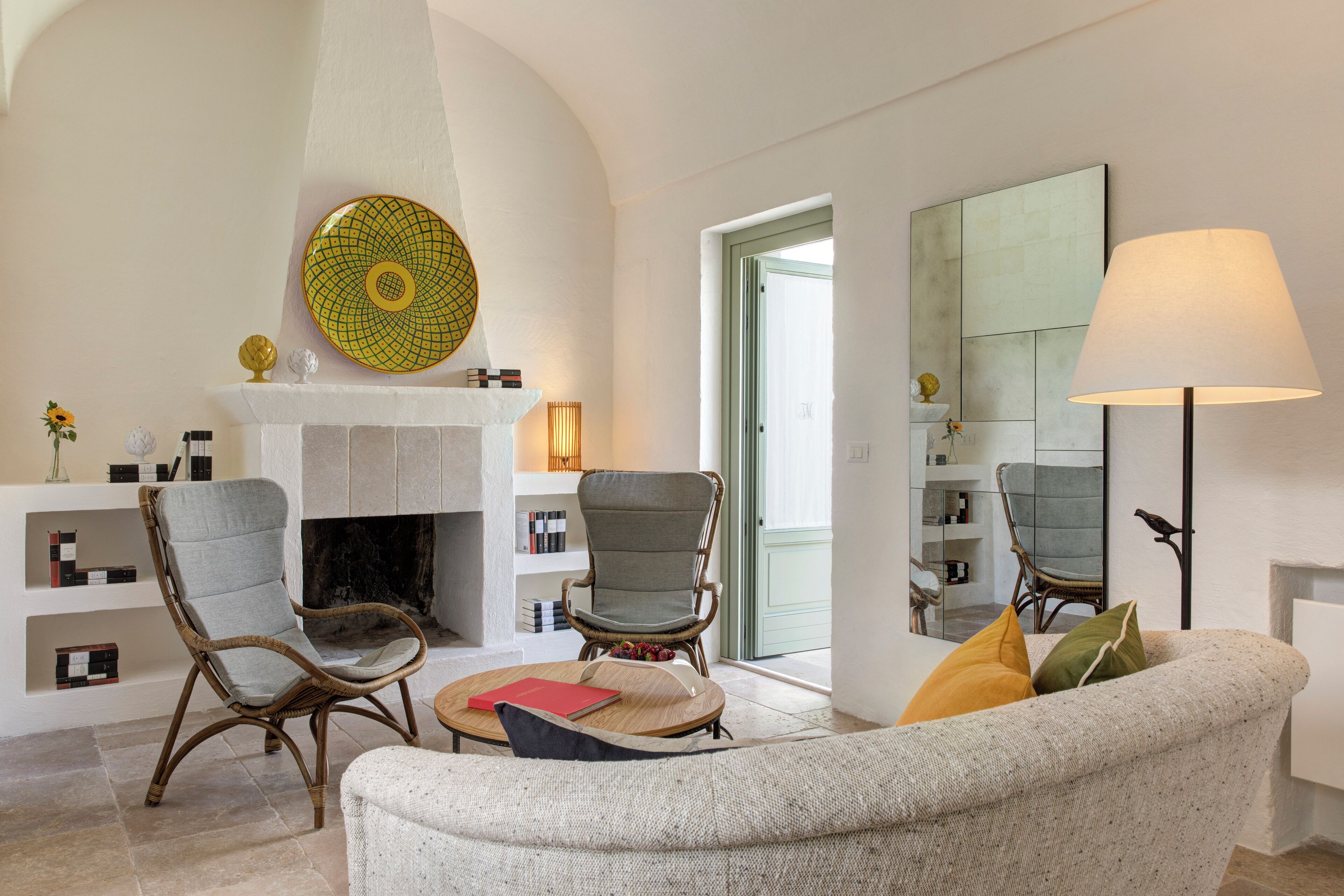 A living room with a fireplace, two wicker chairs, a sofa, and a lamp.