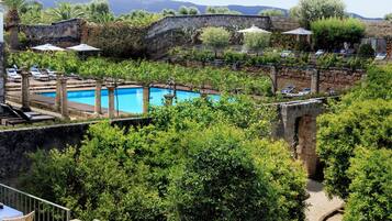 Un área junto a la piscina con mesa y sillas, rodeada de vegetación y vistas a una cadena montañosa.