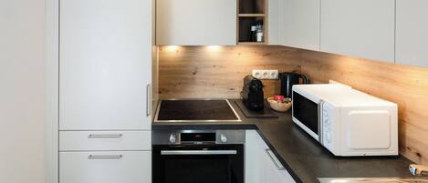 Una cocina compacta con armarios blancos, horno negro, microondas y cafetera.
