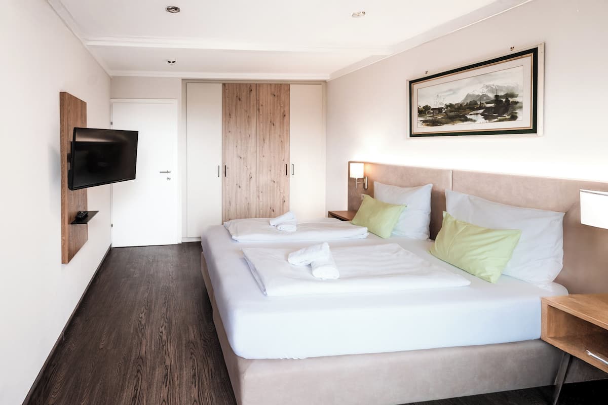 A hotel room with two beds, a TV mounted on the wall, a wooden wardrobe, and a framed picture on the wall.