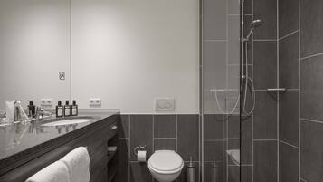 Un baño moderno con ducha envuelta en vidrio, tocador con lavamanos y artículos de aseo, y un inodoro.