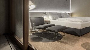 A modern hotel room with a large bed, a small round table with a chair, a bedside lamp, and a large mirror. - Factory Hotel (Münster)
