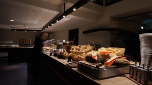A buffet area with various food items and a person serving. - Factory Hotel (Münster)