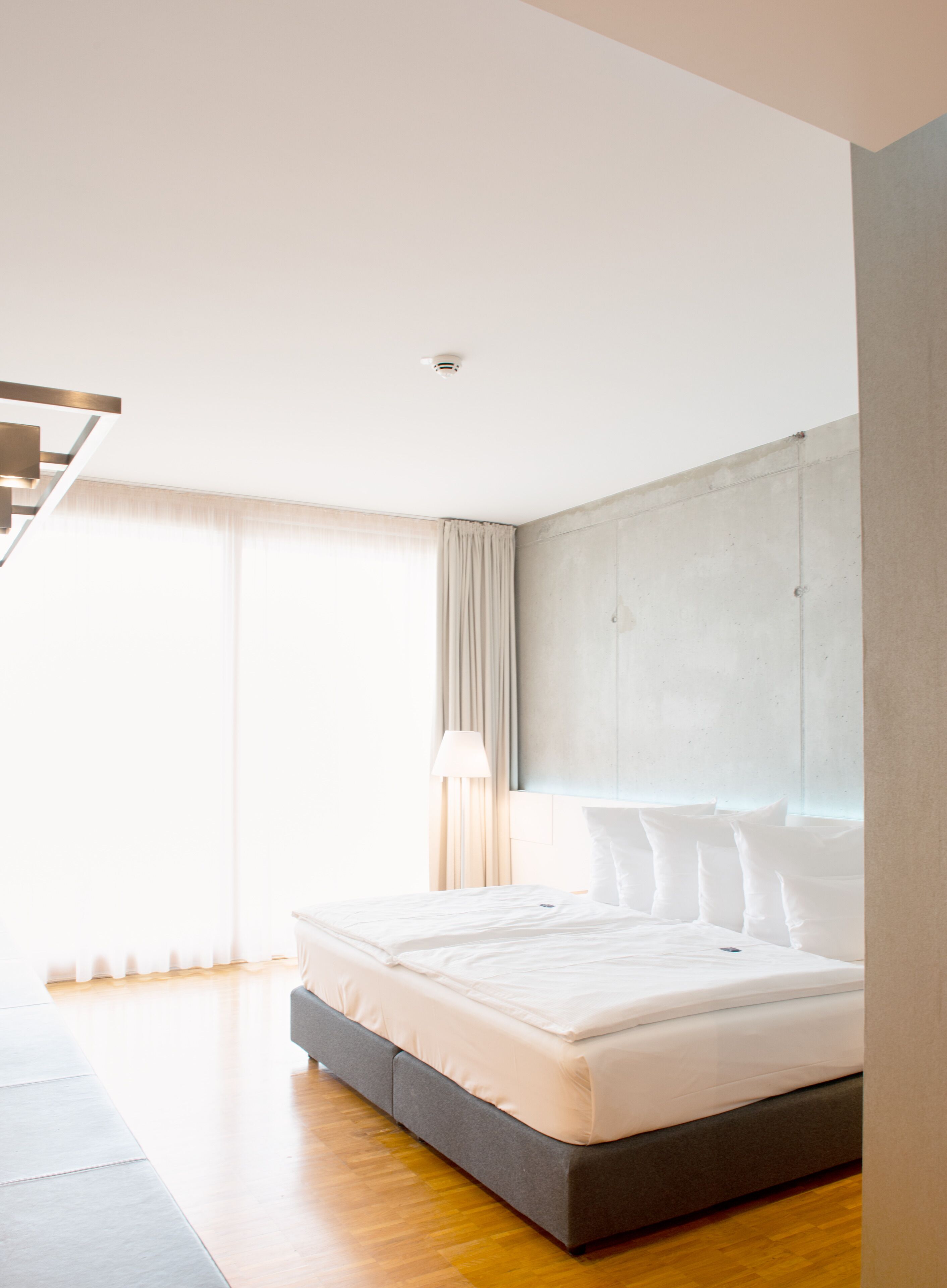 A modern bedroom with a large bed, a headboard, a floor lamp, and a staircase.