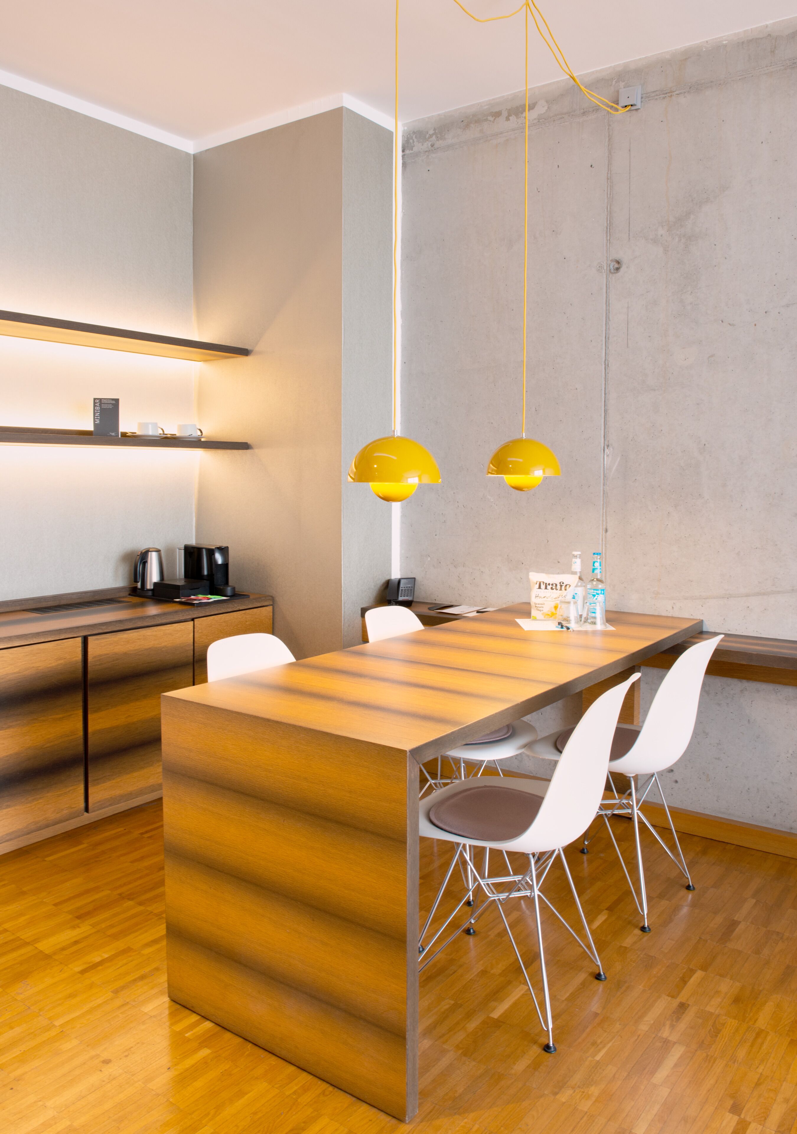A modern kitchen with a wooden island, white chairs, and yellow pendant lights.