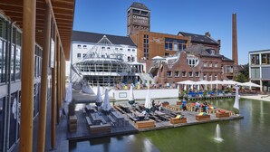 A riverside dock with wooden seating, a glass building, and a brick tower labeled "GERMANIA CAMPUS". - Factory Hotel (Münster)