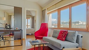Een moderne woonkamer met een grijze bank, een rode fauteuil en grote ramen met uitzicht op de stad.