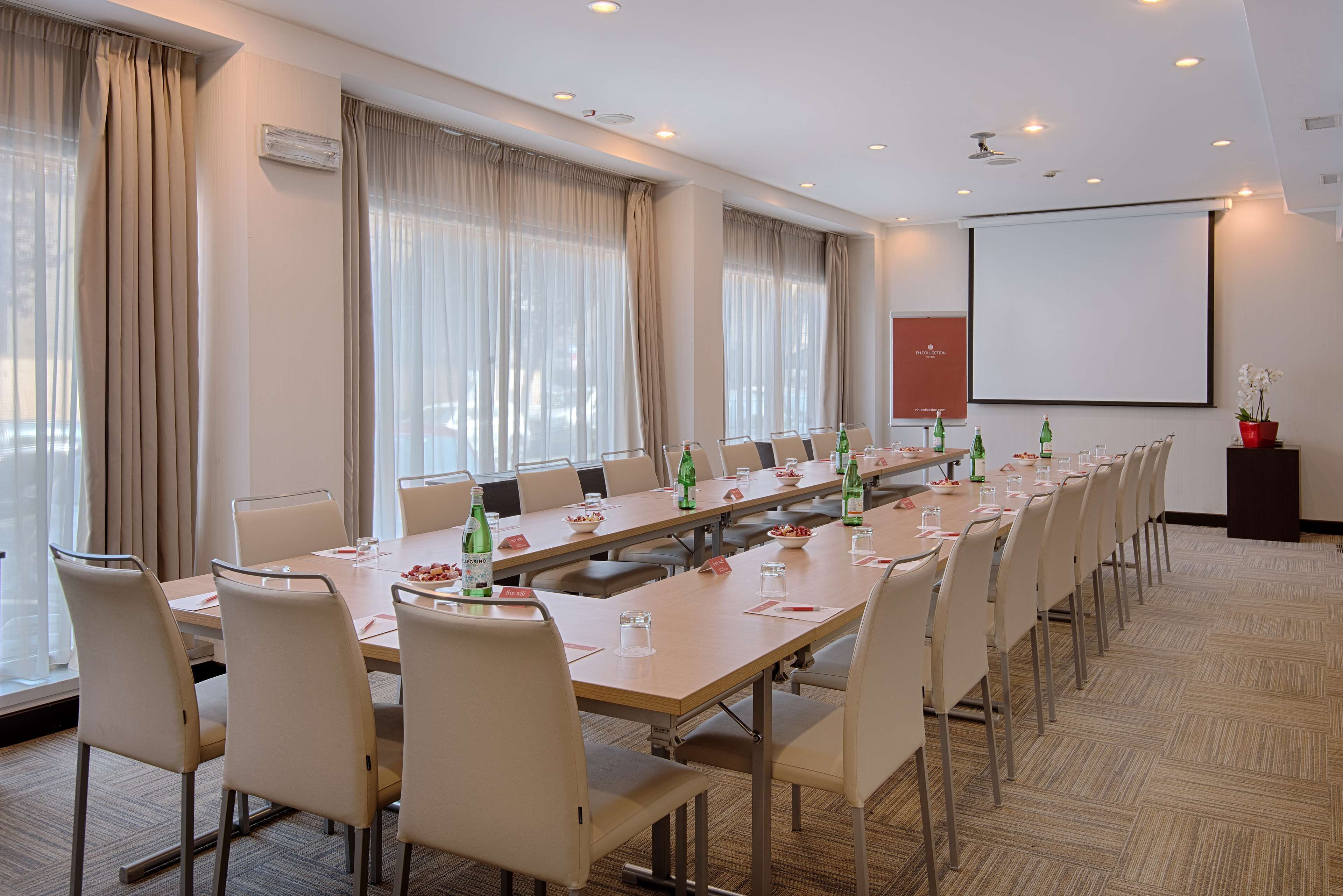 A conference room with a long table, chairs, a projector screen, and a carpeted floor.