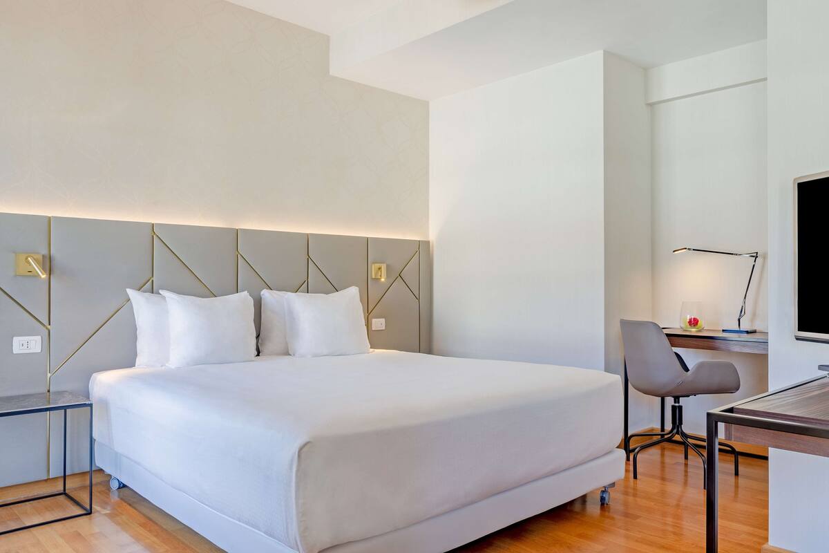 A modern hotel room with a large bed, a desk with a chair, and a flat-screen TV.