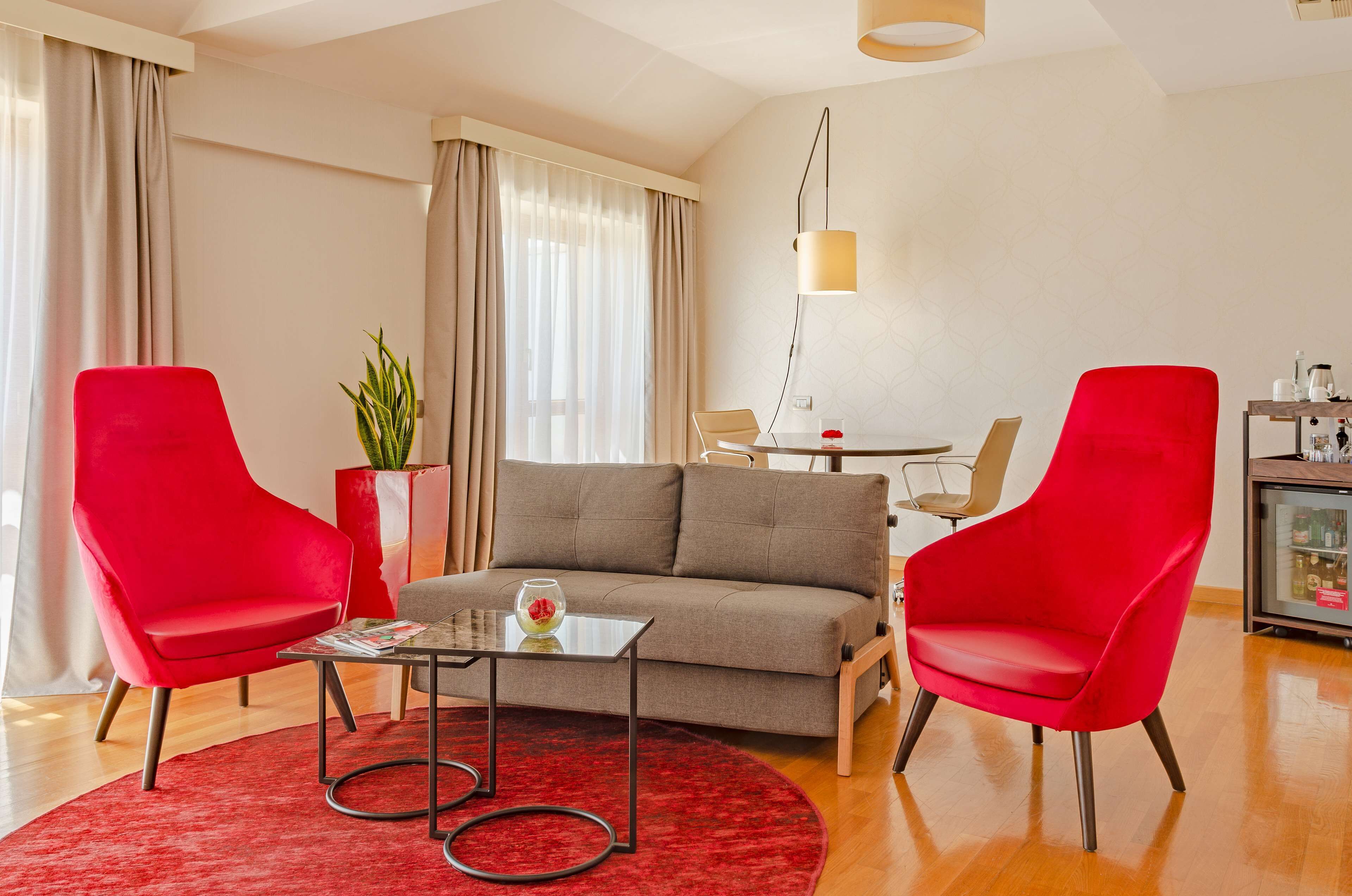 Un salon moderne avec un canapé gris, deux fauteuils rouges, une table basse en verre et un tapis rouge.