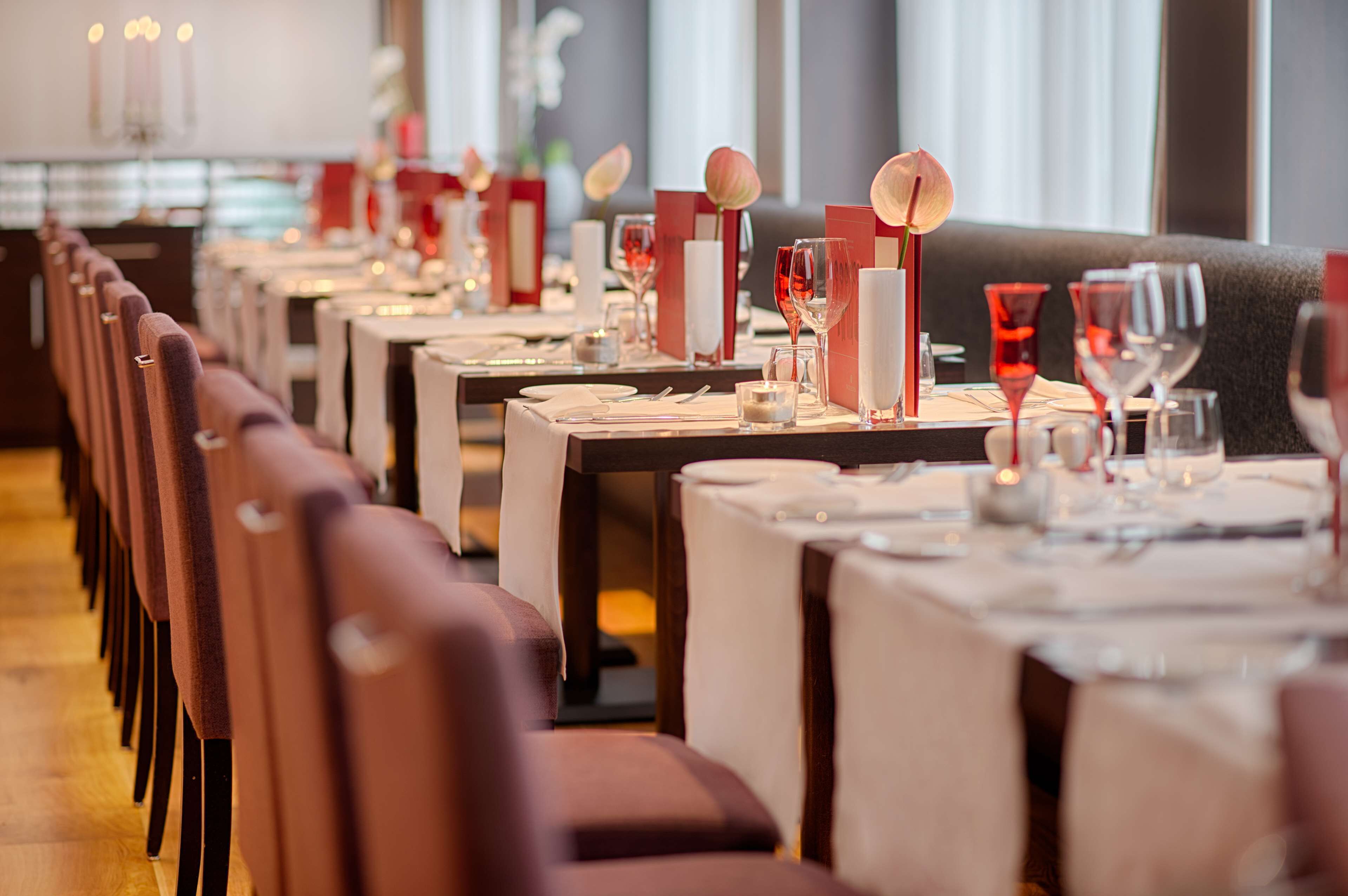 Een restaurant met lange tafels gedekt voor een diner, elk met een kaarsdecoratie, glazen en bestek.