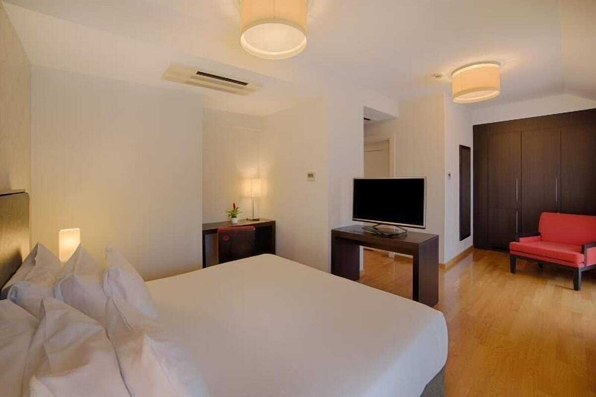 A hotel room with a bed, a TV, a desk, a red chair, and a wardrobe.